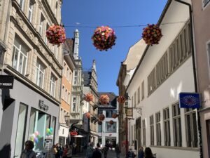 Bild der Fußgängerzone von Konstanz, dekoriert von Neon-Nagel. Mit Dekokugeln die sich Flowwerballs nennen die an einer Straßenüberspannung herunterhängen bestehend aus Sommerblumen.